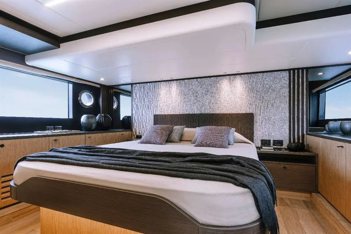 Modern yacht bedroom featuring a double bed with grey cushions, sleek cabinetry, and large windows for natural light.